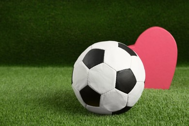 Photo of Soccer ball and heart on green grass. Space for text