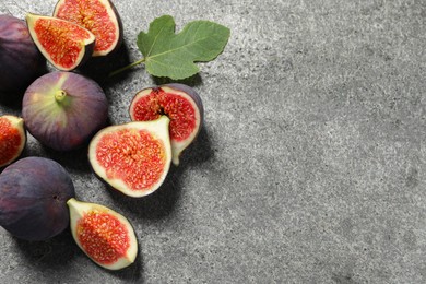 Photo of Whole and cut ripe figs with leaf on grey textured table, flat lay. Space for text