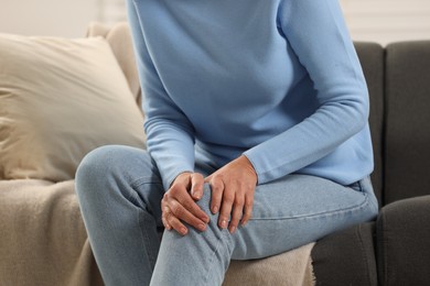 Photo of Mature woman suffering from knee pain on sofa indoors, closeup. Rheumatism symptom