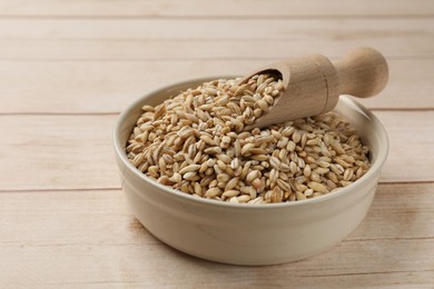 Photo of Dry pearl barley in bowl and scoop on light wooden table, closeup