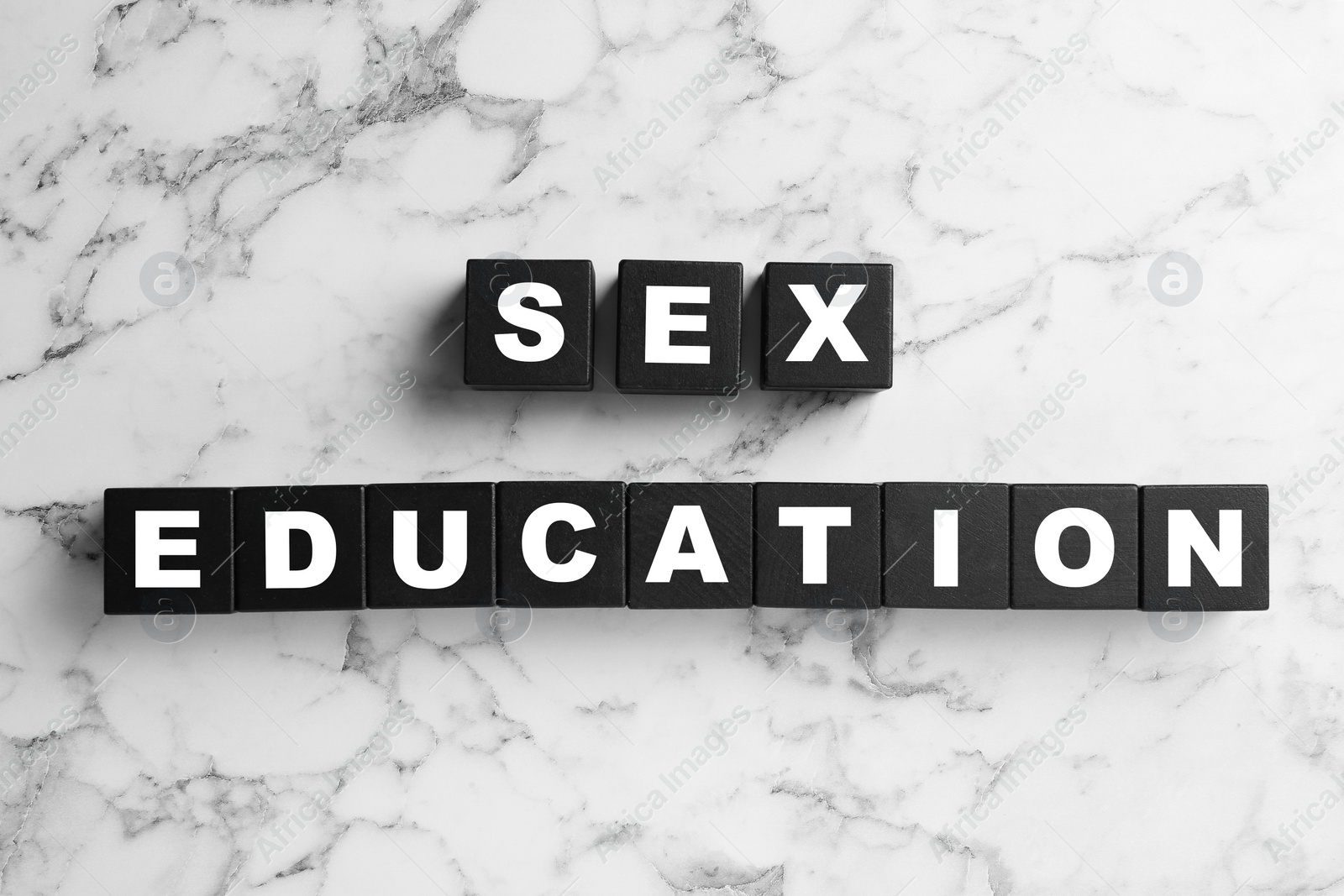 Photo of Black wooden blocks with phrase "SEX EDUCATION" on marble background, flat lay