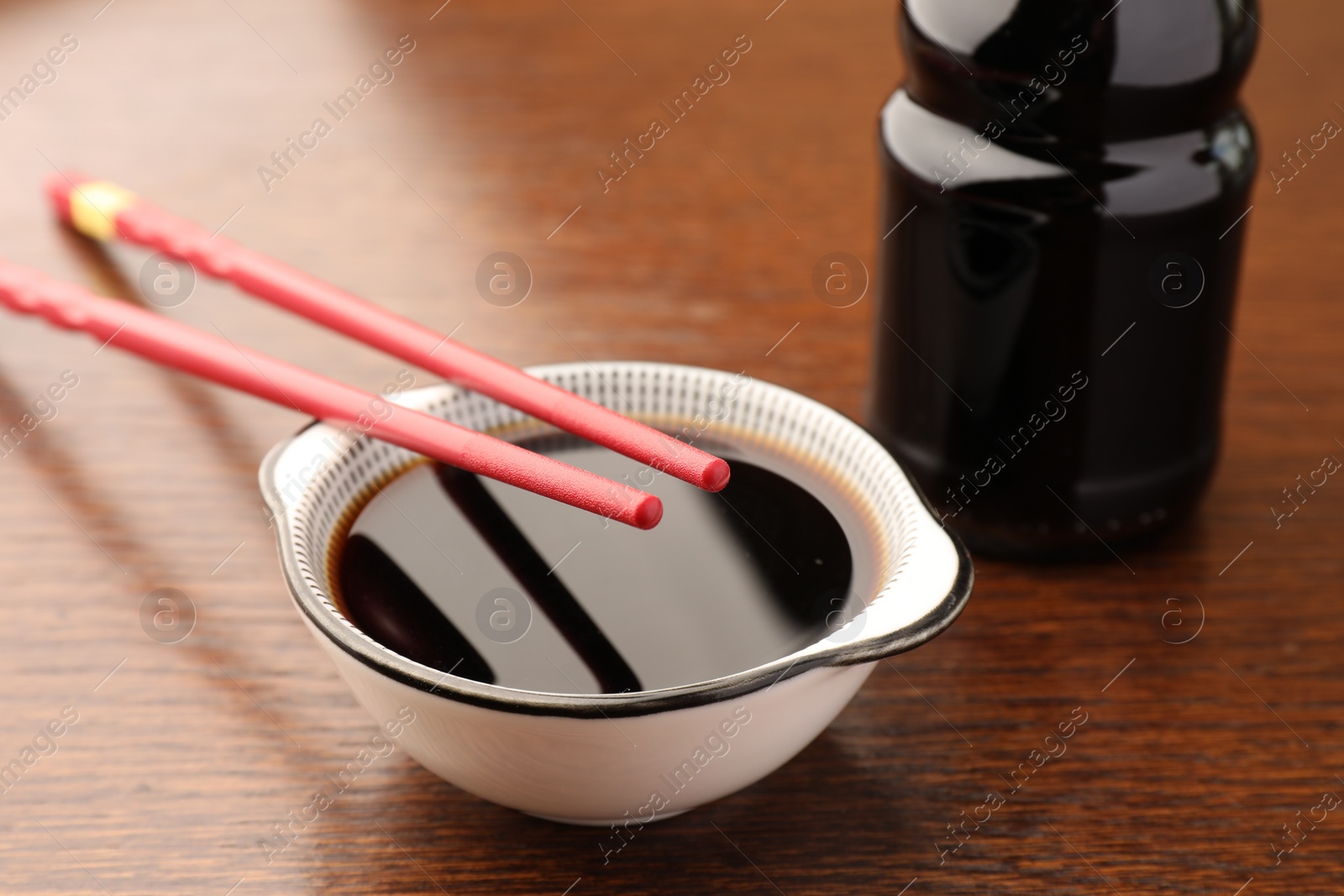 Photo of Bottle, bowl with soy sauce and chopsticks on wooden table, closeup
