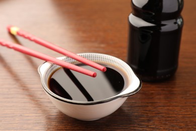 Bottle, bowl with soy sauce and chopsticks on wooden table, closeup