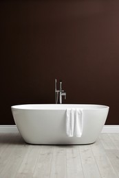 Photo of Modern ceramic bathtub with towel near brown wall indoors