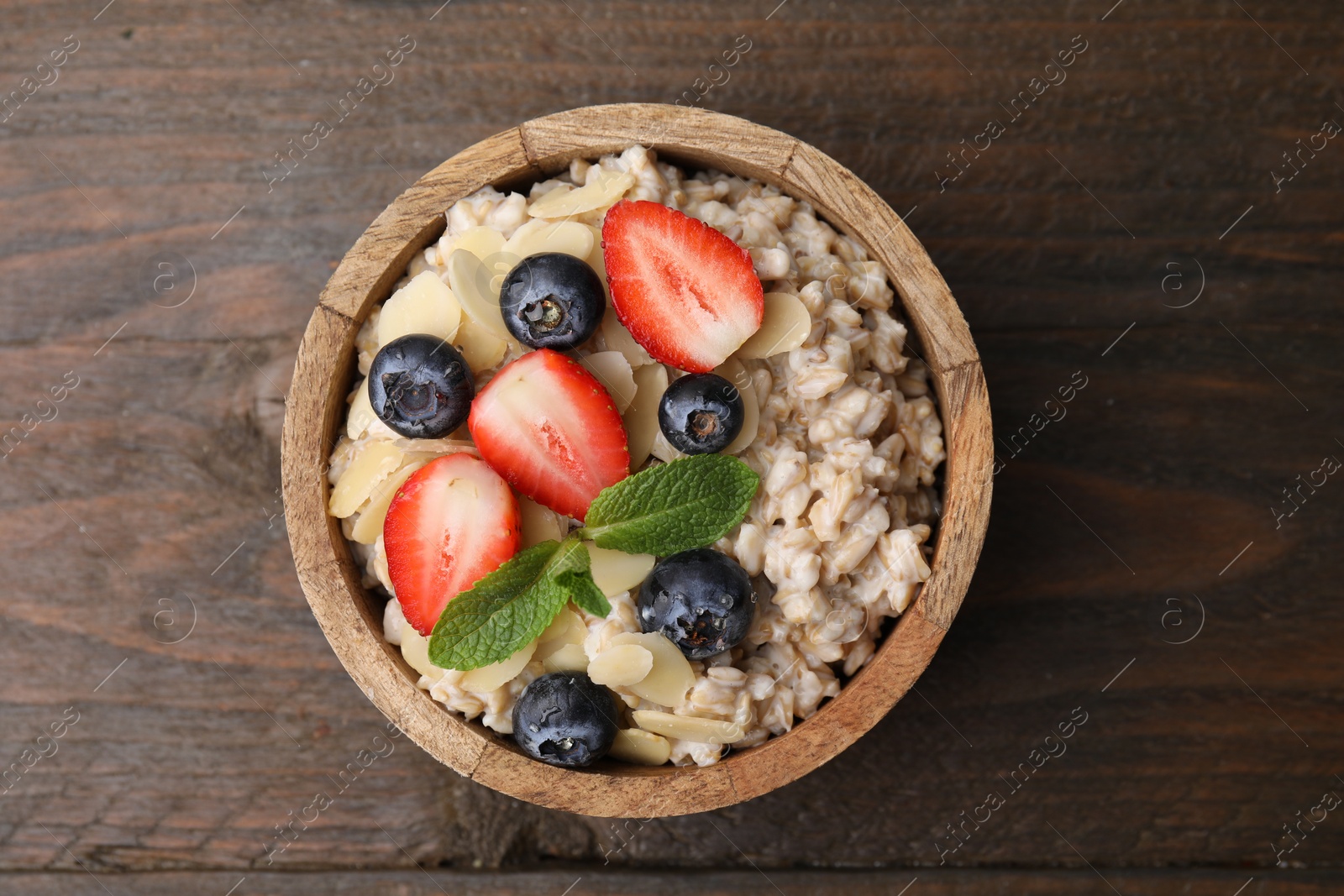 Photo of Tasty oatmeal with strawberries, blueberries and almond flakes in bowl on wooden table, top view