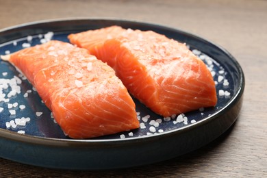 Photo of Fresh raw salmon with salt on wooden table, closeup