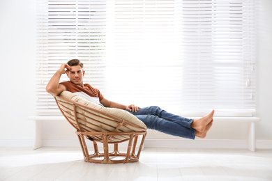 Photo of Attractive man relaxing in papasan chair near window at home