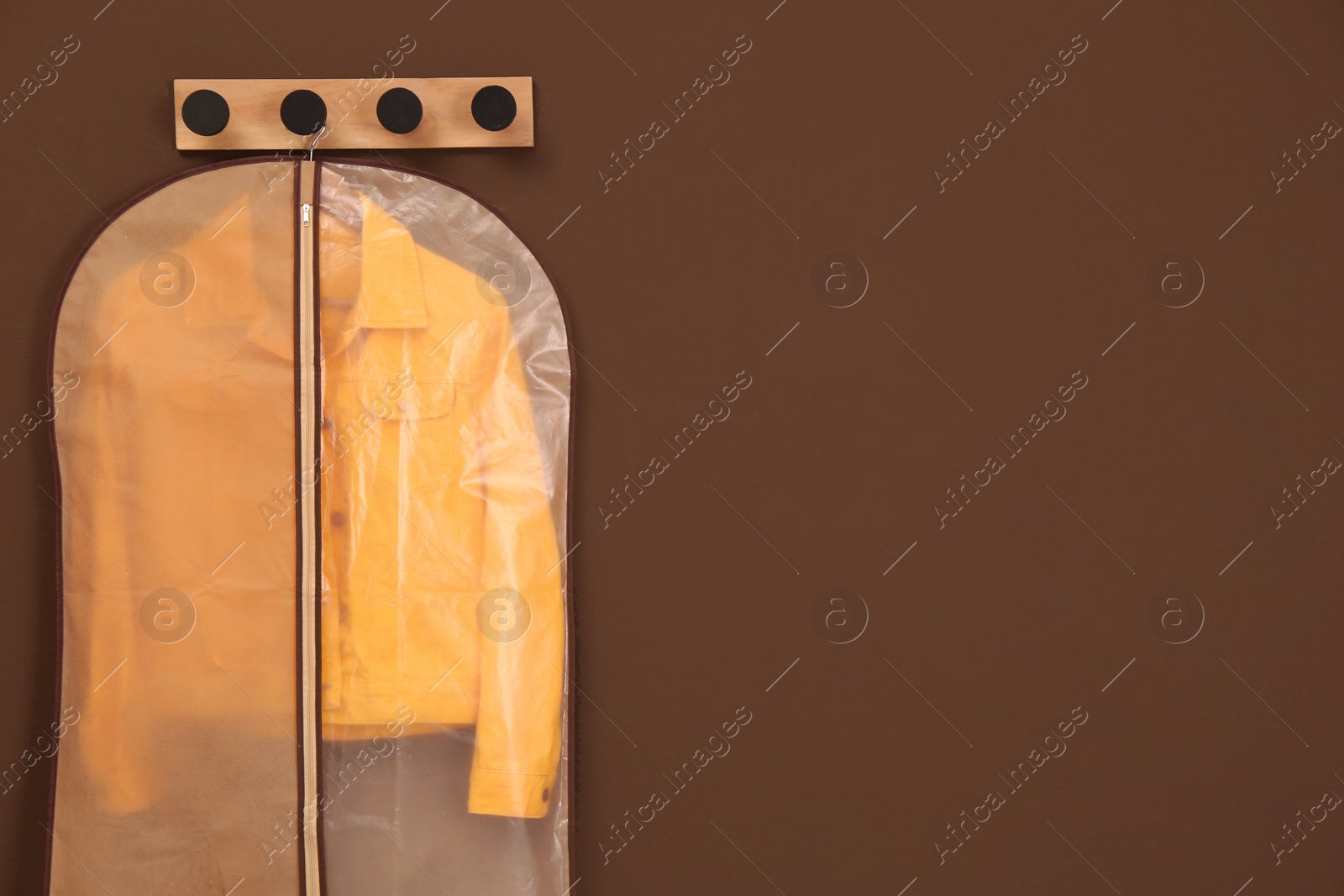 Photo of Garment bag with jacket hanging on brown wall. Space for text