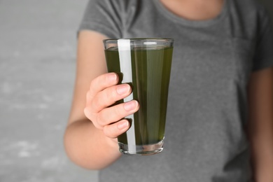 Woman holding glass of spirulina drink on grey background, closeup