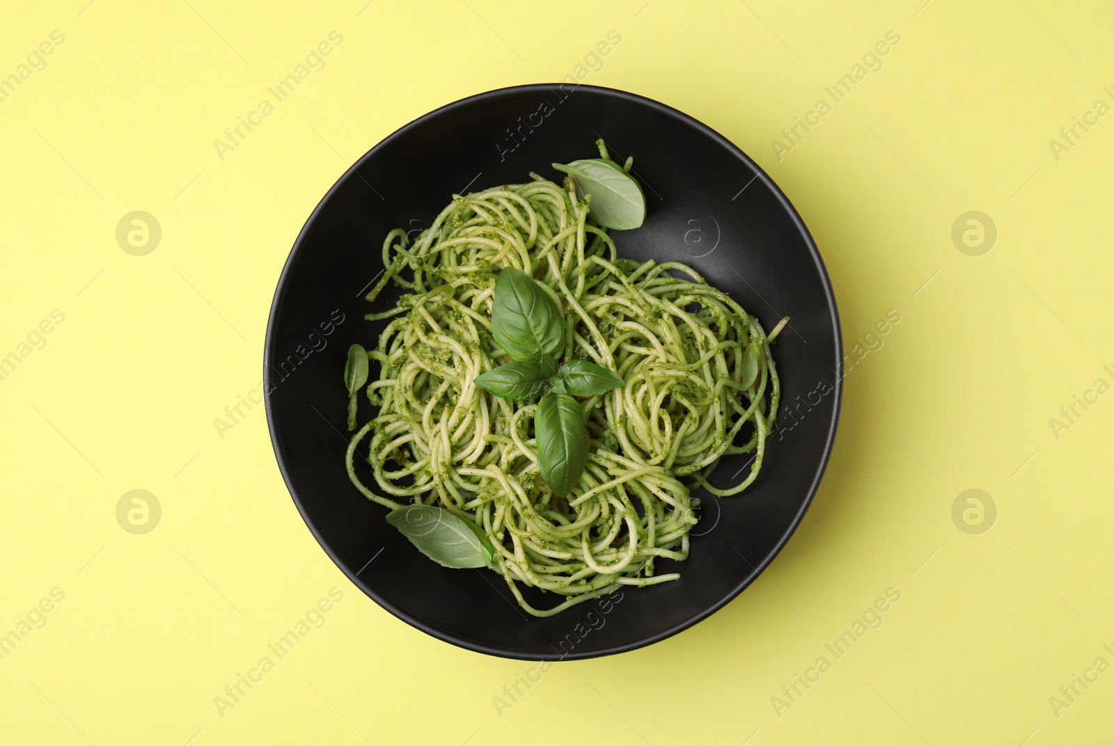 Photo of Delicious pasta with pesto sauce and basil on yellow background, top view