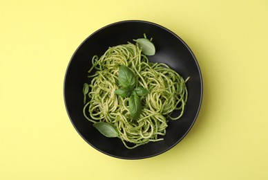 Photo of Delicious pasta with pesto sauce and basil on yellow background, top view