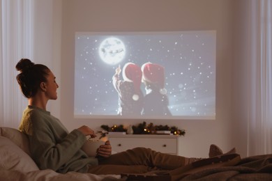 Photo of Woman with popcorn watching Christmas movie via video projector at home