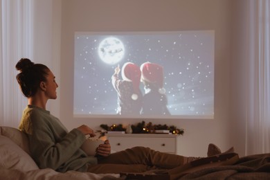 Woman with popcorn watching Christmas movie via video projector at home