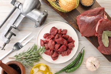 Photo of Metal meat grinder, beef and products on white wooden table, flat lay