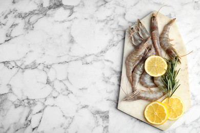 Photo of Raw shrimps with lemon slices and rosemary on marble table, top view. Space for text