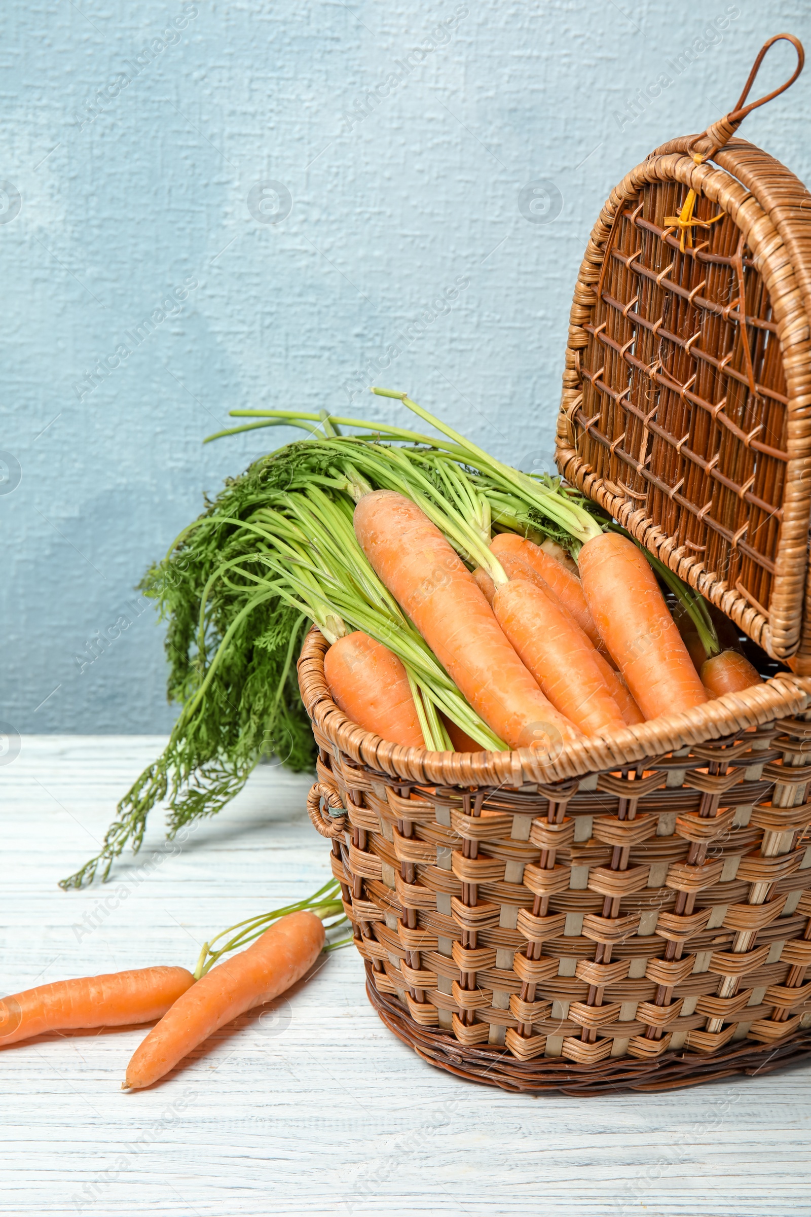 Photo of Wicker basket with ripe carrots on table