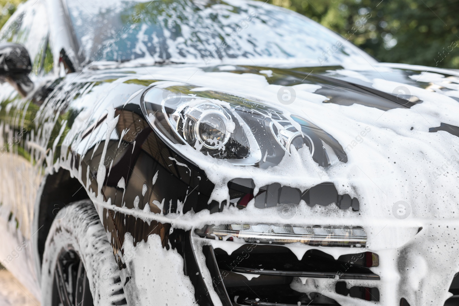 Photo of Auto covered with cleaning foam at outdoor car wash, closeup