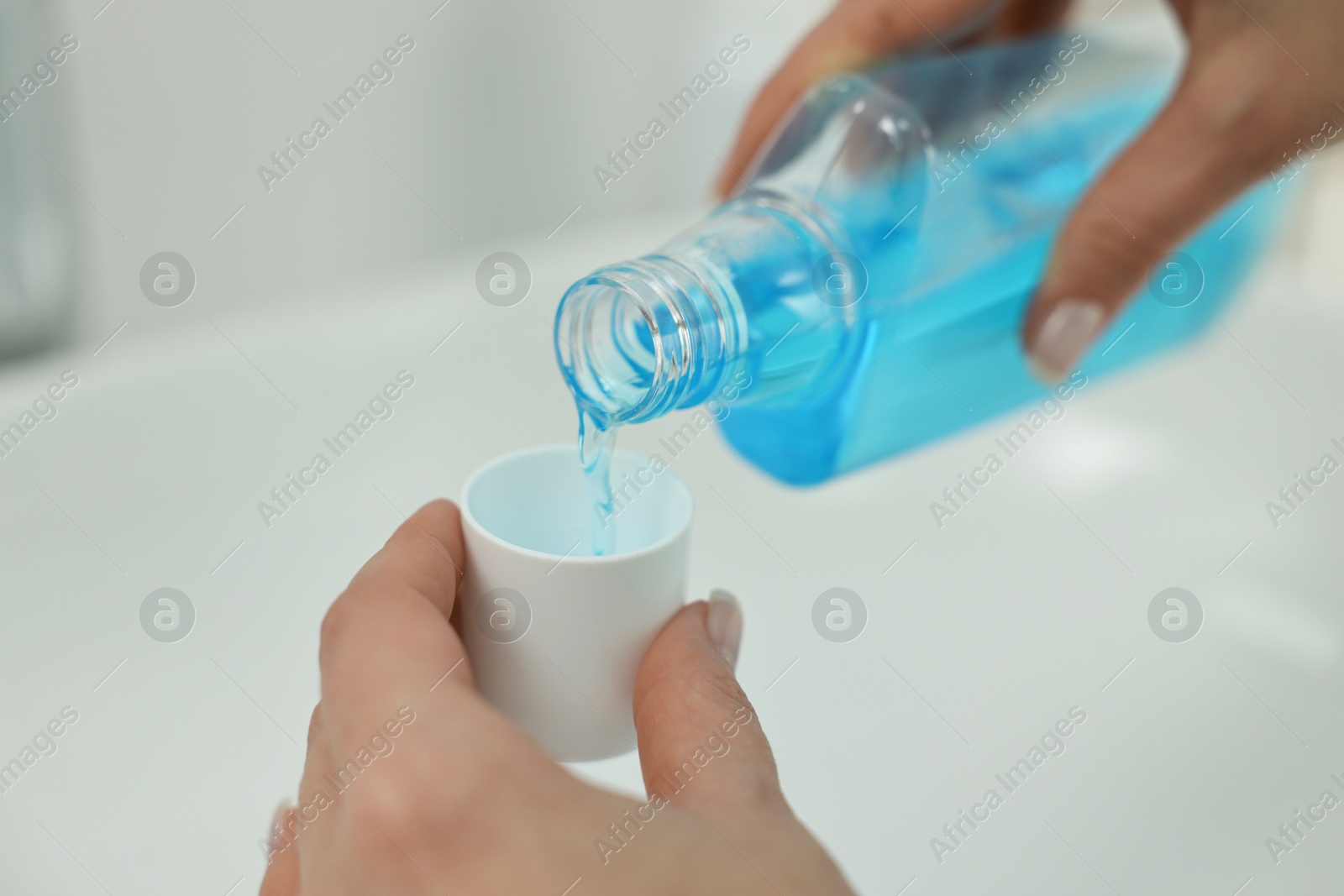 Photo of Young woman using mouthwash above sink in bathroom, closeup