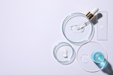 Photo of Petri dishes with samples of cosmetic serums, bottle and pipette on white background, flat lay. Space for text