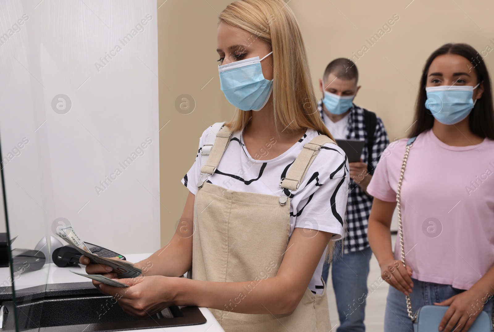 Photo of Woman with protective mask counting money at cash department window in bank. Currency exchange