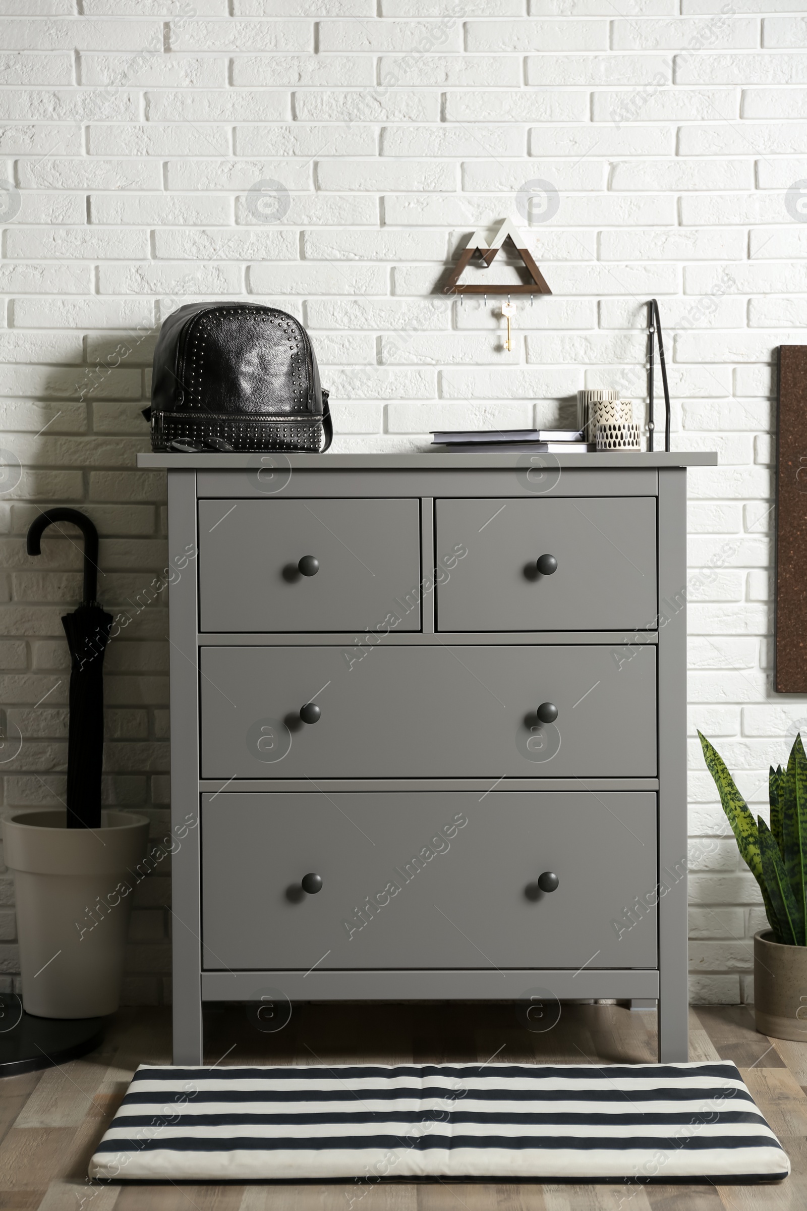 Photo of Grey chest of drawers near white brick wall indoors