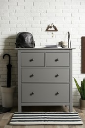 Grey chest of drawers near white brick wall indoors