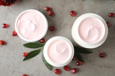 Photo of Jars with natural facial mask, pomegranate seeds and green leaves on light grey table, flat lay