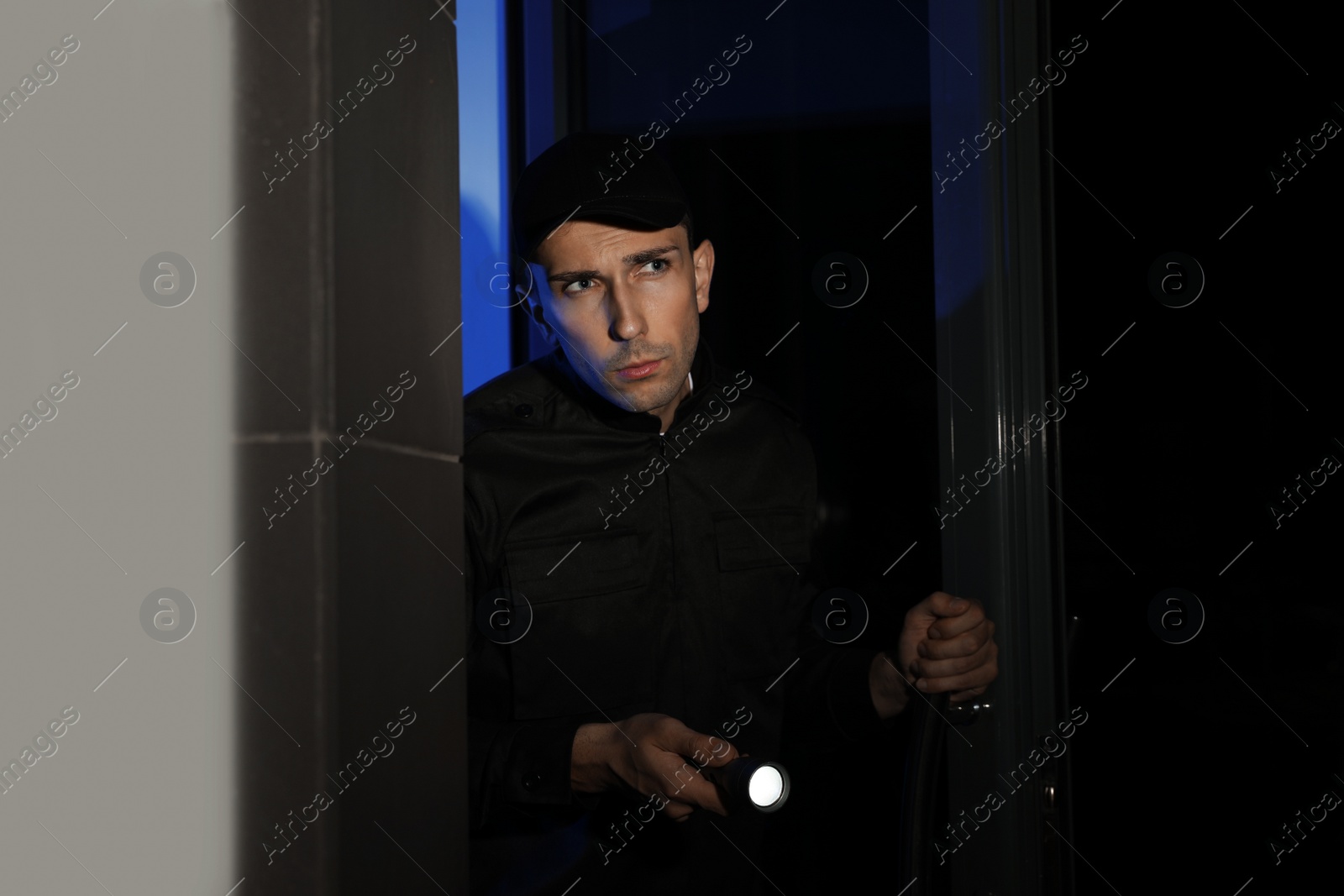 Photo of Male security guard with flashlight near entrance door at night