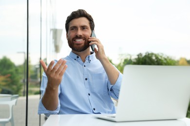 Handsome man with laptop talking on phone in outdoor cafe