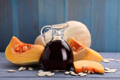 Photo of Fresh pumpkin seed oil in glass jug on grey wooden table