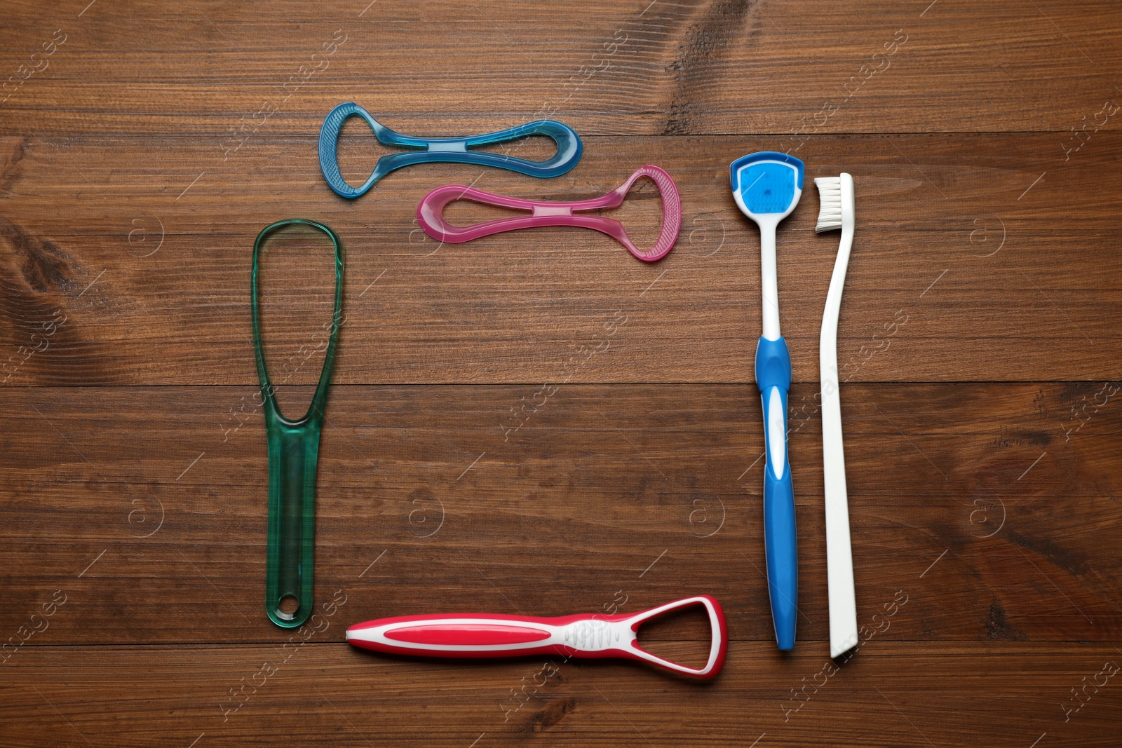 Photo of Frame of different tongue cleaners and toothbrush on wooden table, flat lay. Space for text