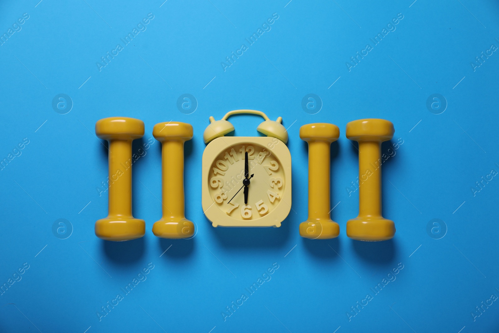 Photo of Yellow alarm clock and dumbbells on light blue background, flat lay. Morning exercise