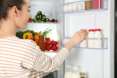 Photo of Young woman taking yoghurt out of refrigerator, closeup