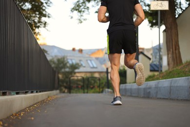 Photo of Attractive sporty man in fitness clothes jogging outdoors, closeup
