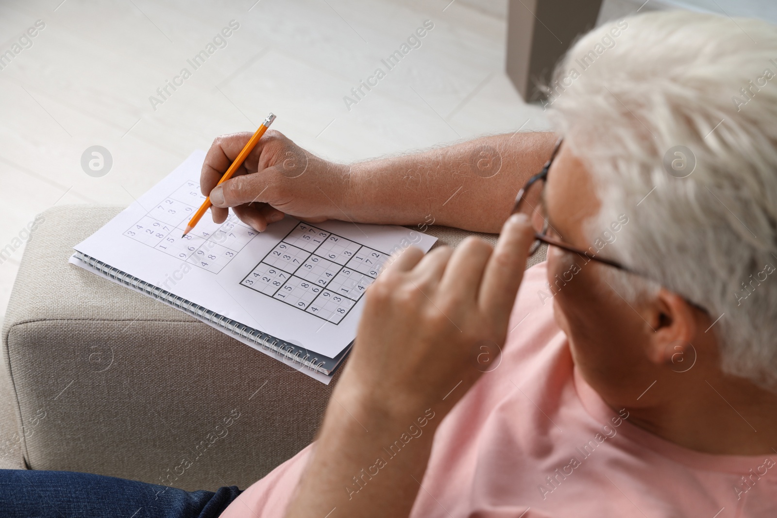Photo of Senior man solving sudoku puzzle on sofa at home