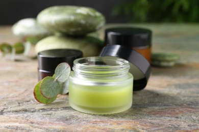 Photo of Jars of cream and eucalyptus leaves on textured table, closeup. Body care products