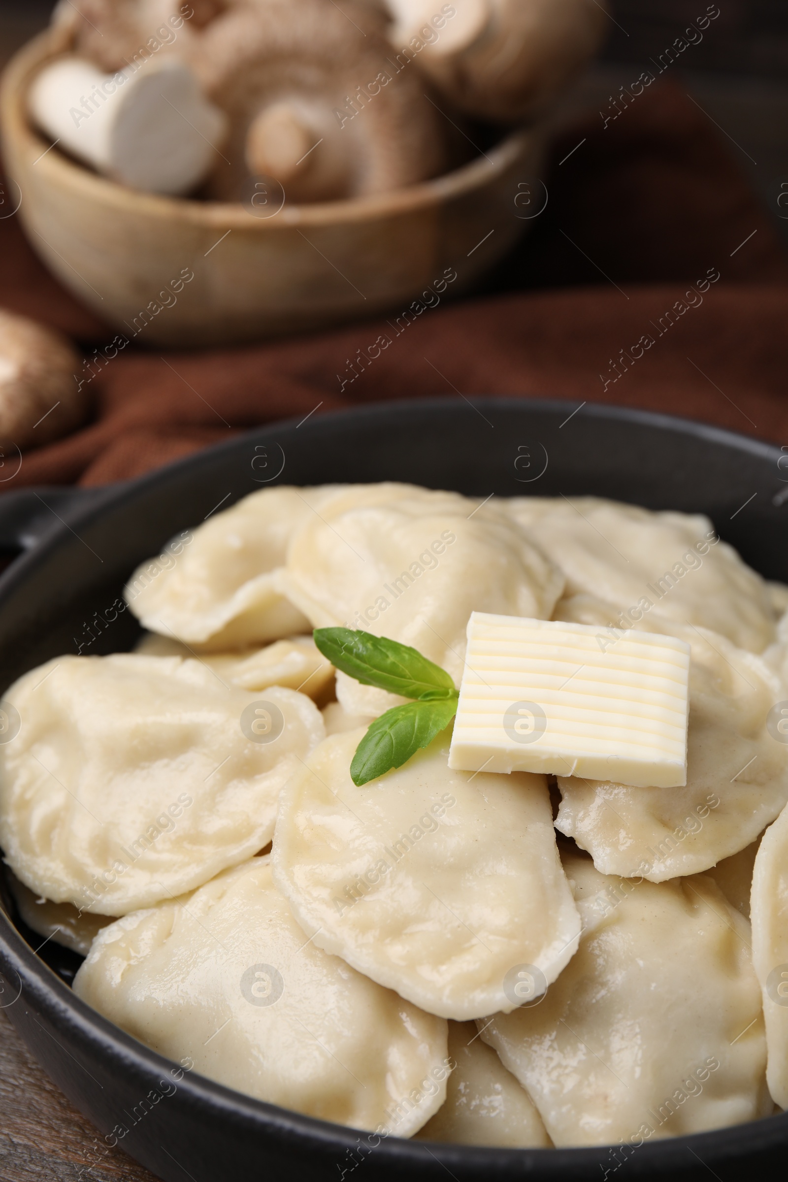 Photo of Serving pan of delicious dumplings (varenyky) with mushrooms on wooden table, closeup