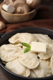 Photo of Serving pan of delicious dumplings (varenyky) with mushrooms on wooden table, closeup