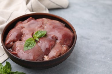 Photo of Bowl with raw chicken liver and basil on light grey table, closeup. Space for text