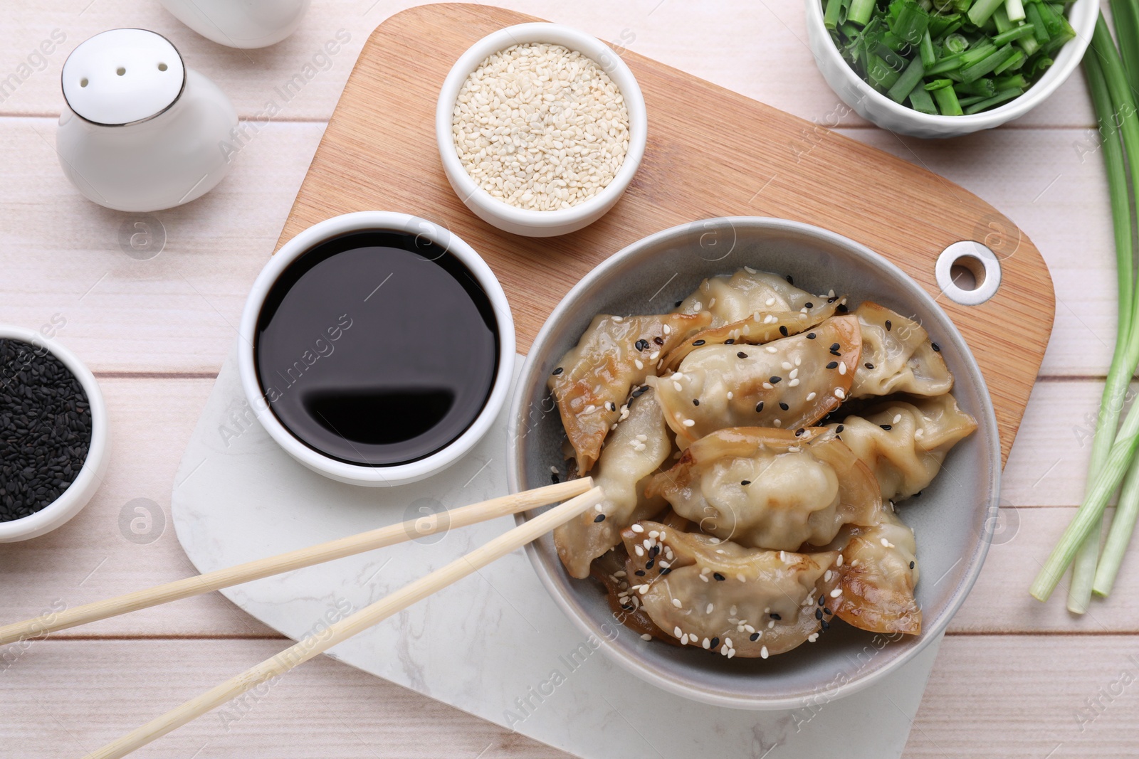 Photo of Delicious gyoza (asian dumplings), soy sauce and sesame on white wooden table, flat lay