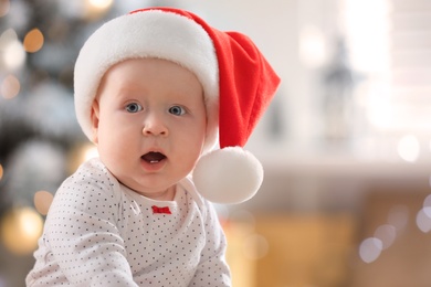 Photo of Little baby wearing Santa hat indoors. First Christmas