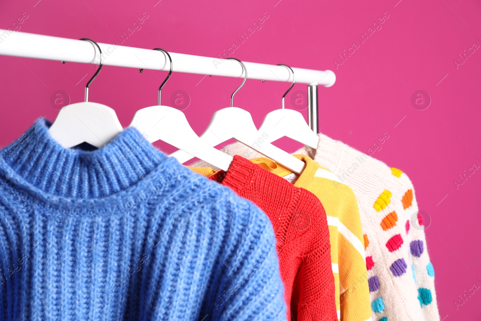 Photo of Collection of warm sweaters hanging on rack against color background, closeup