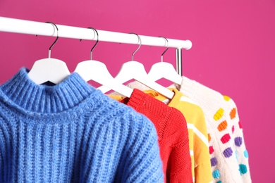 Collection of warm sweaters hanging on rack against color background, closeup