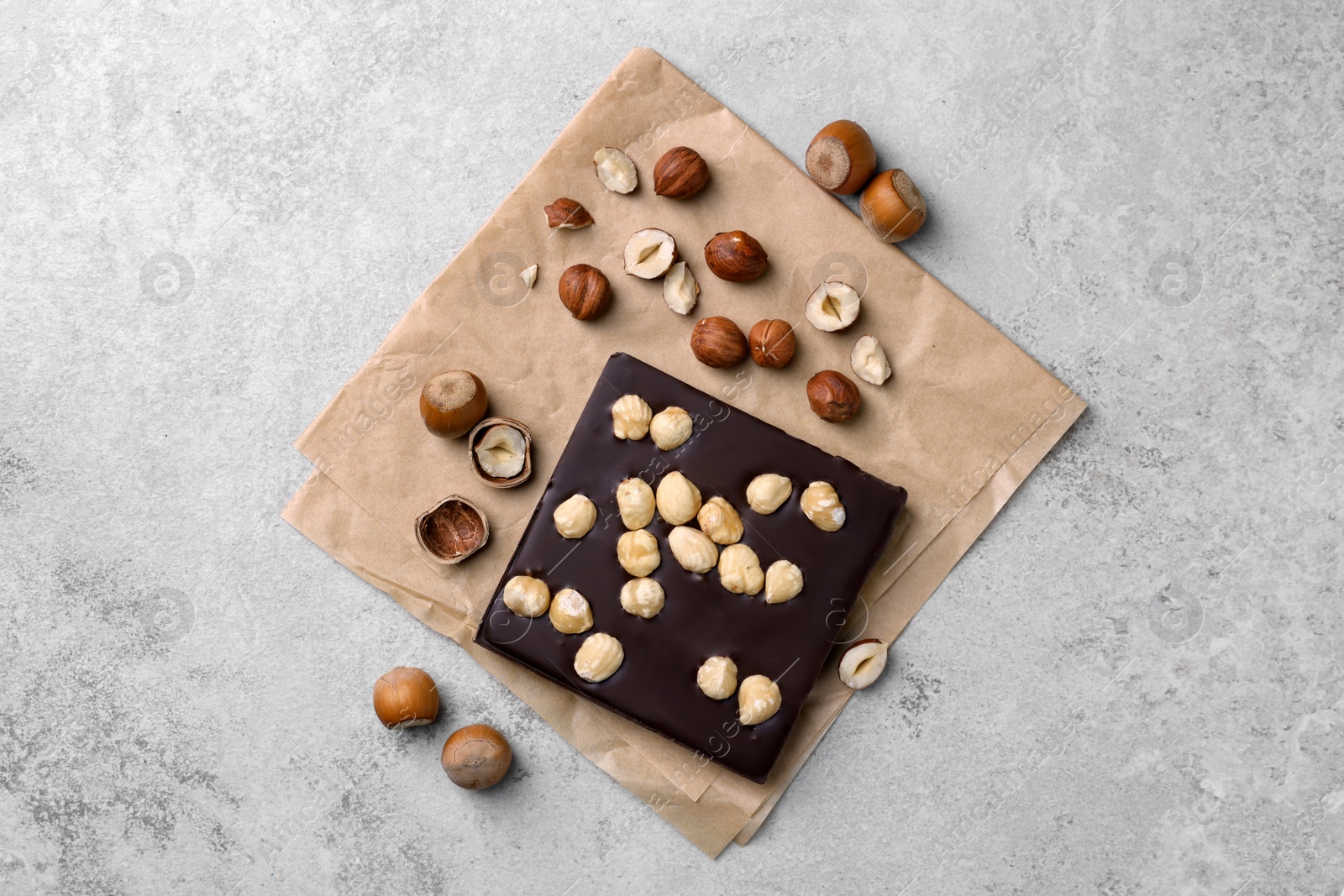 Photo of Delicious chocolate bar and hazelnuts on light grey table, flat lay