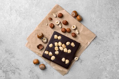 Delicious chocolate bar and hazelnuts on light grey table, flat lay