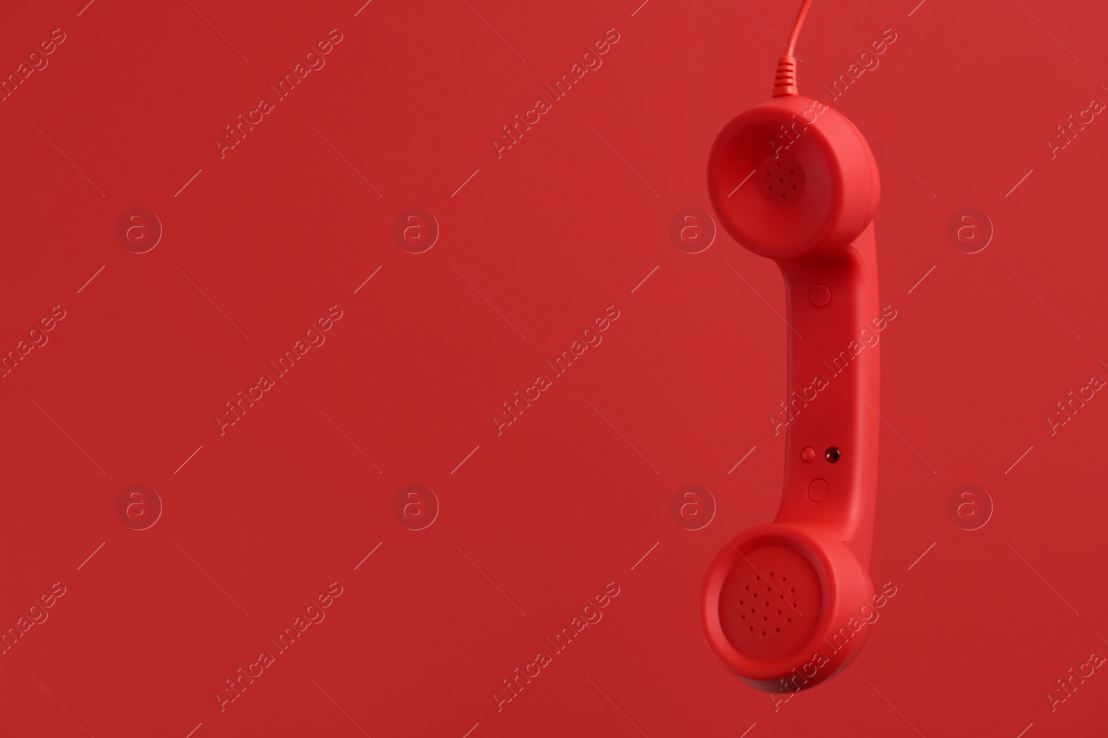 Photo of Corded telephone handset hanging on red background, space for text. Hotline concept