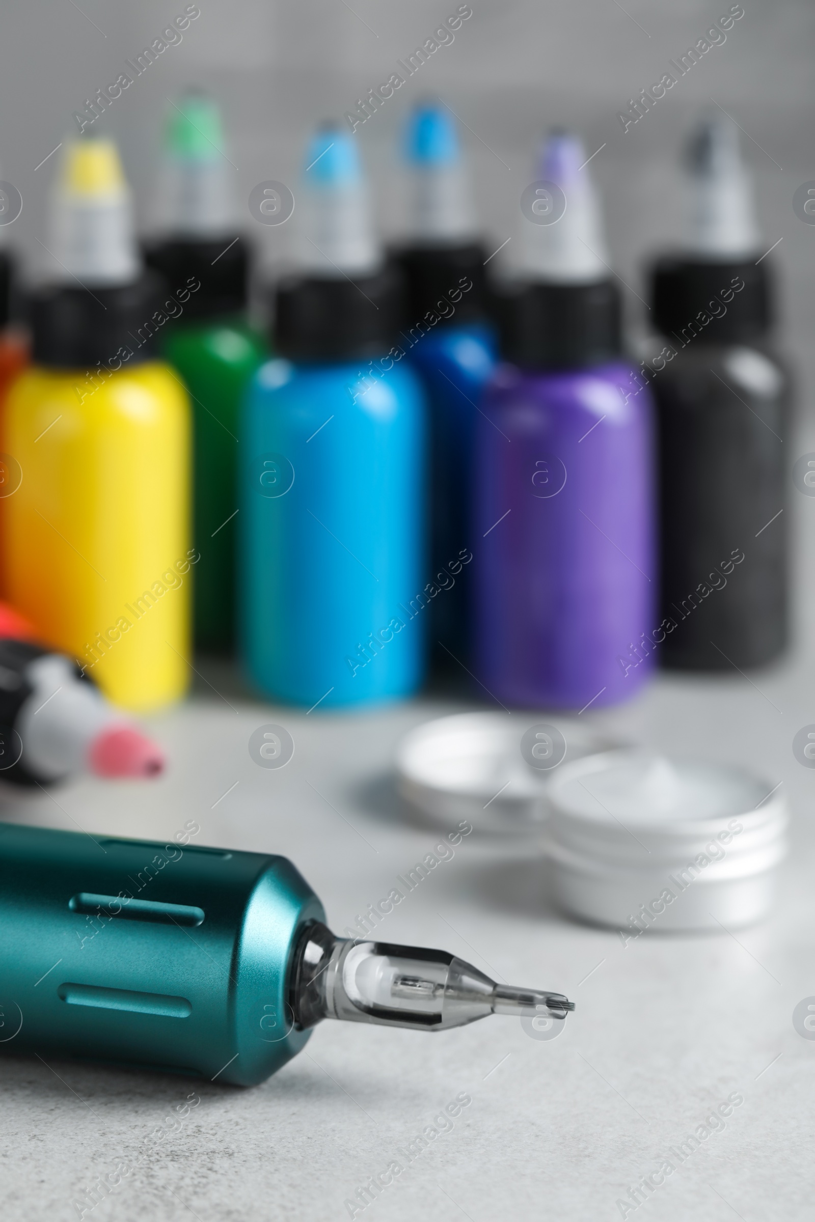 Photo of Modern professional tattoo machine and colorful inks on white table, space for text