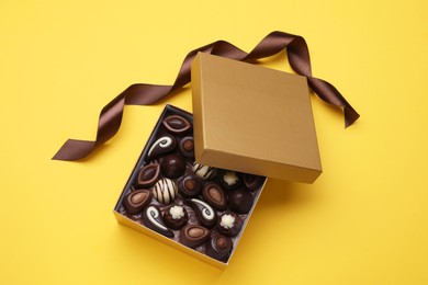 Photo of Open box of delicious chocolate candies on yellow background, flat lay