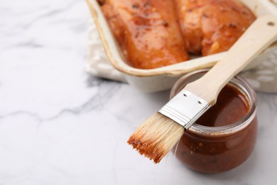 Photo of Fresh marinade, basting brush and raw chicken fillets on white table, closeup. Space for text