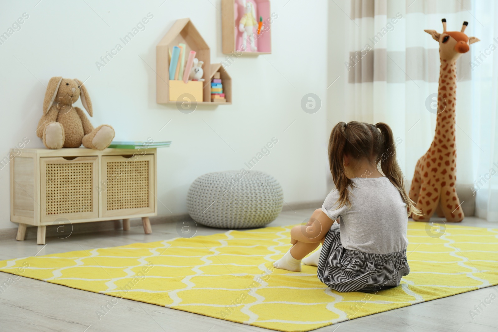 Photo of Lonely little girl sitting on floor at home, back view. Autism concept